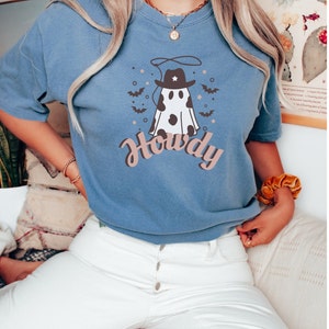 May include: A blue t-shirt with a white ghost wearing a cowboy hat and the word "Howdy" printed on it.