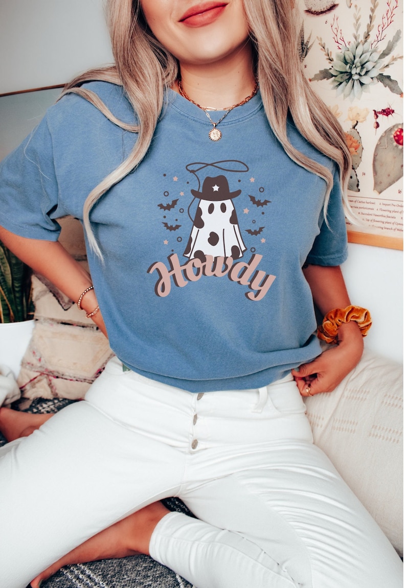 May include: A blue t-shirt with a white ghost wearing a cowboy hat and the word "Howdy" printed on it.
