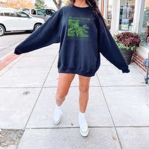 May include: A black sweatshirt with a green graphic print of a Monstera Deliciosa plant. The text "Monstera Deliciosa" is printed in white above the graphic.