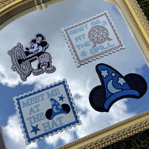 May include: Four embroidered patches featuring a silver and blue color scheme. One patch shows a mouse at a ship wheel, another a wizard hat, and two rectangular stamp-shaped patches with the text Meet Me At The Ball and Meet Me At The Hat.
