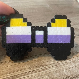 May include: A black and white pixel art bow tie with yellow, white, and purple stripes. The bow tie is made of small plastic beads.