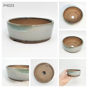 May include: A ceramic bonsai pot with a light grey exterior and a brown interior. The pot has a rounded oval shape with a slight turquoise glaze around the rim. The bottom is a darker brown colour. The text "P4023" is visible in the upper left corner.