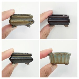 Peut inclure: Quatre petits pots à bonsaï en céramique de différentes couleurs : marron, marron foncé et bleu-vert. Chaque pot a une forme rectangulaire avec des bords arrondis et de petits pieds. Les pots sont tenus par une main.