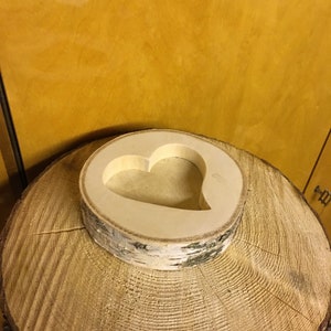 May include: A wooden heart-shaped cutout on a round wooden base. The base is made of birch wood and has a natural bark texture.