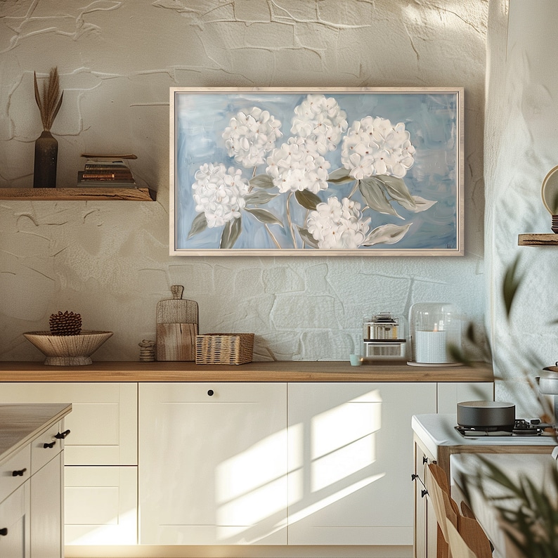 May include: A framed painting of white hydrangeas on a blue background. The painting is hanging on a white wall in a kitchen.
