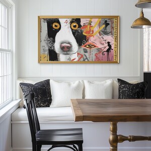 Peut inclure: Une œuvre d'art encadrée représentant un gros plan du visage d'un chien avec des yeux jaunes, un pelage noir et blanc et un nez rose. L'arrière-plan comprend des éléments abstraits en rose, jaune et noir, avec un cadre doré. L'œuvre est au-dessus d'une table.