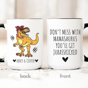May include: White ceramic mug with a black handle and rim. One side features a cartoon dinosaur wearing sunglasses and a bandana. The other side reads "DON'T MESS WITH MAMASAURUS YOU'LL GET JURASSKICKED."