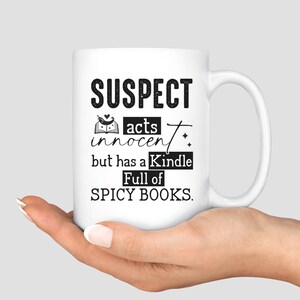 May include: White ceramic mug with black text that reads "SUSPECT acts innocent but has a Kindle full of SPICY BOOKS."
