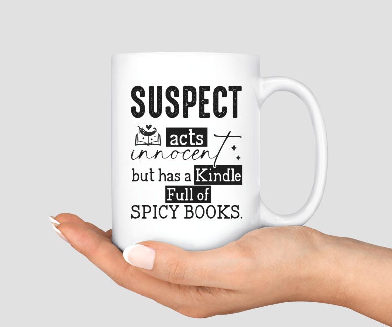 May include: White ceramic mug with black text that reads "SUSPECT acts innocent but has a Kindle full of SPICY BOOKS."