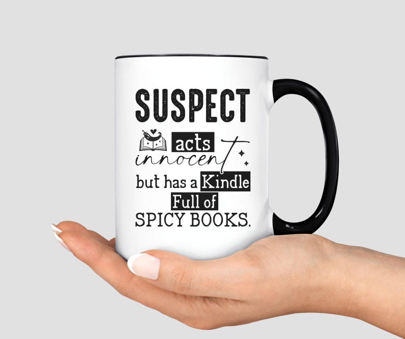 May include: White coffee mug with a black rim and handle. The mug has black text that reads "SUSPECT acts innocent but has a Kindle Full of SPICY BOOKS."