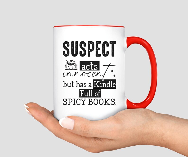 May include: White coffee mug with a red rim and handle. The mug has black text that reads "SUSPECT acts innocent but has a Kindle Full of SPICY BOOKS."