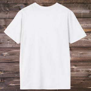 Puede incluir: Una camiseta blanca lisa de manga corta. La camiseta est&aacute; hecha de un material suave y opaco. La camiseta se muestra sobre un fondo de madera r&uacute;stica de color marr&oacute;n oscuro.