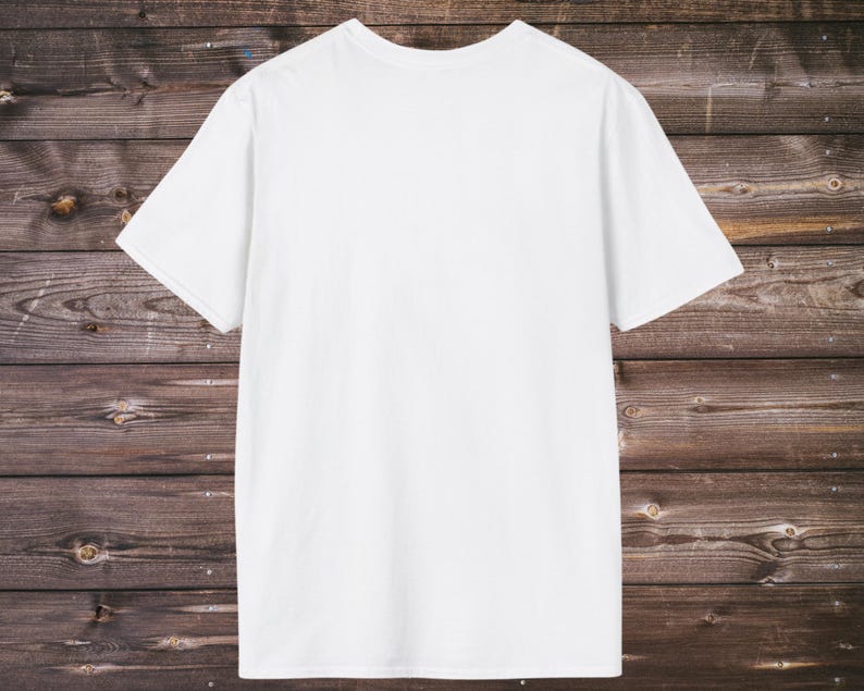 Puede incluir: Una camiseta blanca lisa de manga corta. La camiseta est&aacute; hecha de un material suave y opaco. La camiseta se muestra sobre un fondo de madera r&uacute;stica de color marr&oacute;n oscuro.