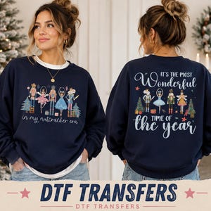 May include: A navy blue crewneck sweatshirt featuring a graphic of nutcracker characters and ballet dancers with the text "in my nutcracker era" on the front and "IT'S THE MOST Wonderful TIME OF THE year" with nutcracker figures on the back.
