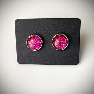 May include: A pair of silver stud earrings with pink glitter embedded in the center of each earring.