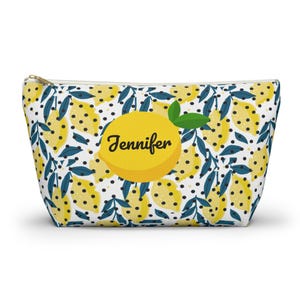 Può includere: Un astuccio con cerniera con un motivo a limoni. Il design presenta limoni gialli con punti neri, foglie blu e il nome "Jennifer" su una grande grafica di limone. L'astuccio ha uno sfondo bianco.