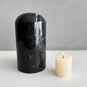 May include: A black marble cylinder candle holder with a white candle inside. The candle is lit and the flame is visible.