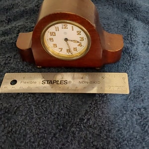 May include: A small, wooden, mantel clock with a white face and gold-coloured hands. The clock has Roman numerals and a star in the centre of the face.