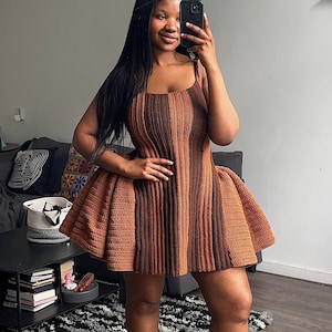 Peut inclure: Robe au crochet marron et beige avec un col carré et une jupe évasée. La robe est faite d'un fil texturé et a un corsage ajusté. La robe arrive au genou et est portée avec des talons bruns.