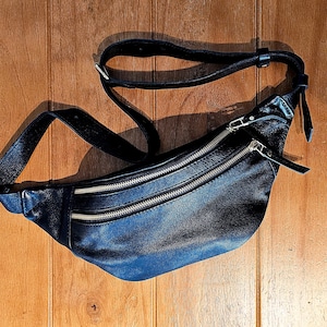 May include: A black leather fanny pack with two zippered compartments and a long adjustable strap.