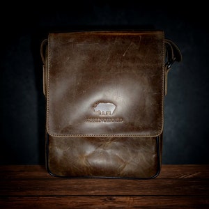 K&ouml;nnte beinhalten: Eine braune Ledertasche mit einem Nashorn-Logo und dem Schriftzug "RHINO HOLD" auf der Vorderseite.