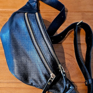 May include: A black leather fanny pack with gold zippers and a long adjustable strap.