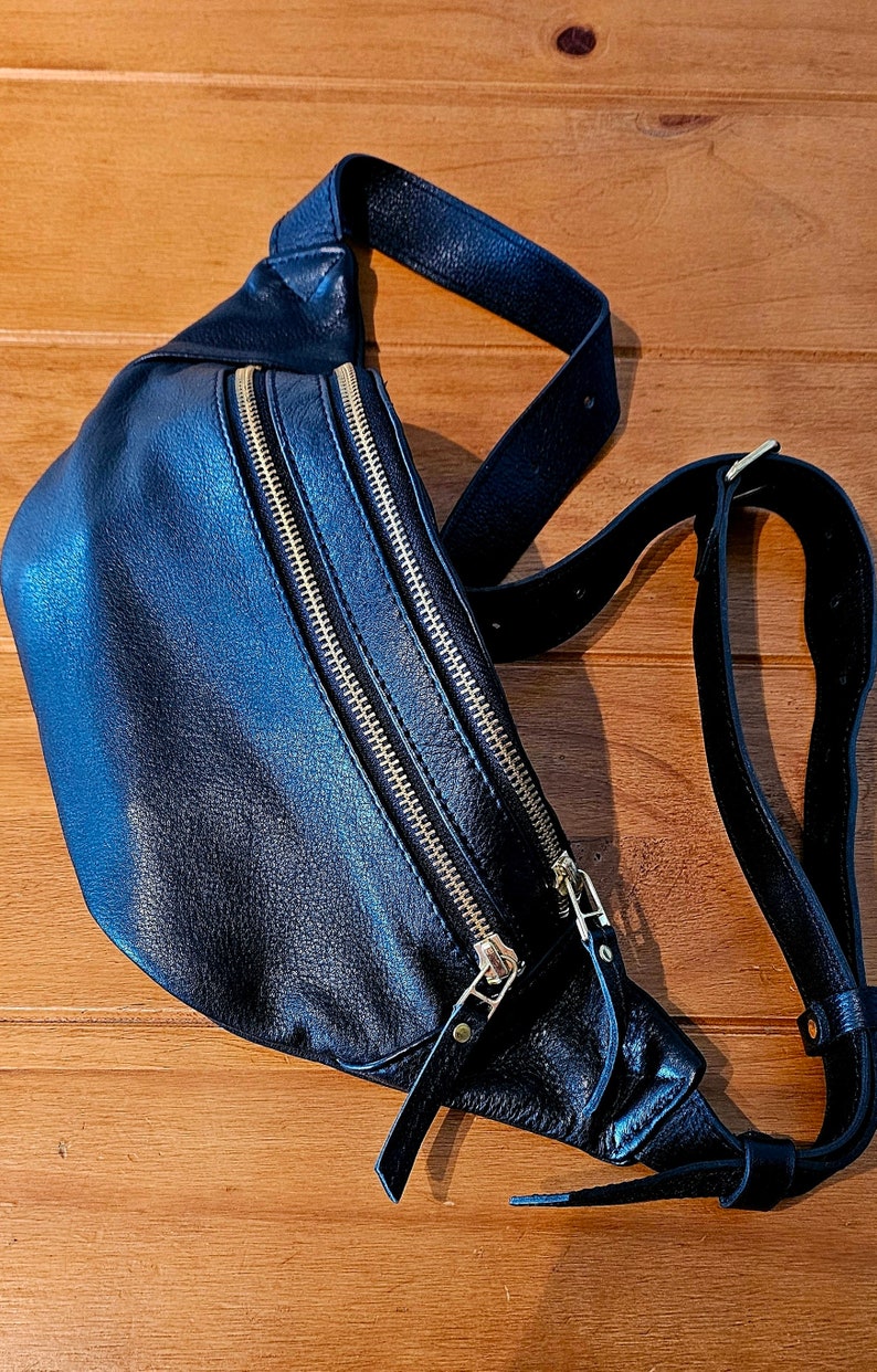 May include: A black leather fanny pack with gold zippers and a long adjustable strap.