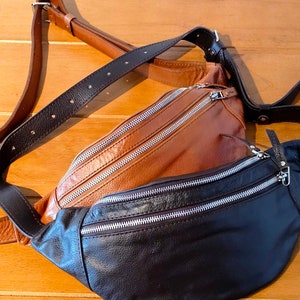 May include: A brown leather fanny pack with a black leather fanny pack attached to it. Both have silver zippers.