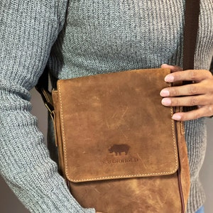 K&ouml;nnte beinhalten: Eine braune Ledertasche mit einem gesteppten Klappdeckel und einem Nashorn-Logo mit der Aufschrift "RhinoHold".