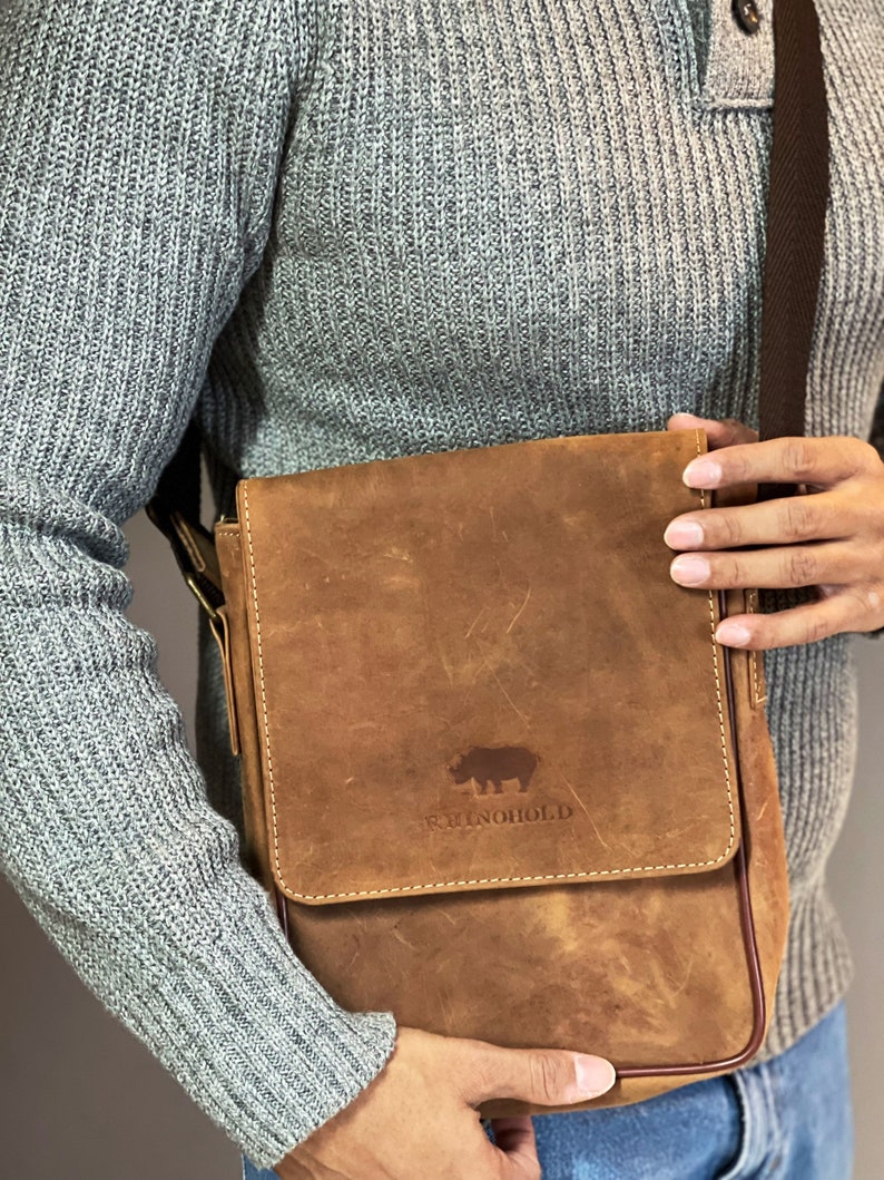 K&ouml;nnte beinhalten: Eine braune Ledertasche mit einem gesteppten Klappdeckel und einem Nashorn-Logo mit der Aufschrift "RhinoHold".