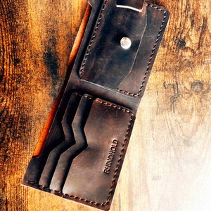 Può includere: Un portafoglio in pelle marrone con più slot per carte e un fermaglio per banconote. Il portafoglio ha la scritta "RHINO HOLD" impressa sul davanti.