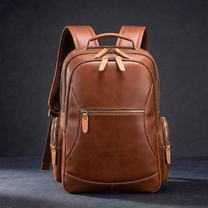 May include: A medium brown leather backpack featuring a large main compartment with double zips, a smaller front zipped pocket, and two side zipped pockets. The bag includes a top handle and adjustable shoulder straps with metal hardware.