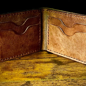 Peut inclure: Un portefeuille en cuir marron avec deux fentes pour cartes de chaque c&ocirc;t&eacute;, ouvert et pos&eacute; sur une surface en bois.