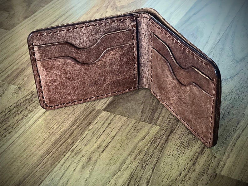 Peut inclure: Un portefeuille en cuir marron avec plusieurs emplacements pour cartes et un porte-billets. Le portefeuille est ouvert et l'int&eacute;rieur est visible.