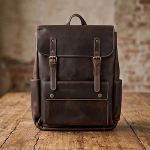 May include: A dark brown leather backpack featuring a top handle, a fold-over flap with two vertical straps, and brass-toned metal buckles. The front includes a rectangular pocket with a flap closure, and there are two side pockets.