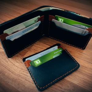 May include: Black leather wallet with brown detailing and orange stitching, open to reveal card slots holding various cards. A smaller matching cardholder is also shown, displaying a TD Access Card.
