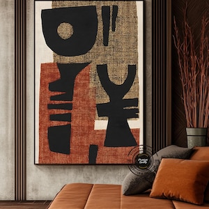 May include: Abstract art print featuring bold black shapes on a textured gold and rust-colored background. The artwork is framed in a black border and hangs above a brown leather sofa with matching throw pillows. The overall aesthetic is modern and minimalist.