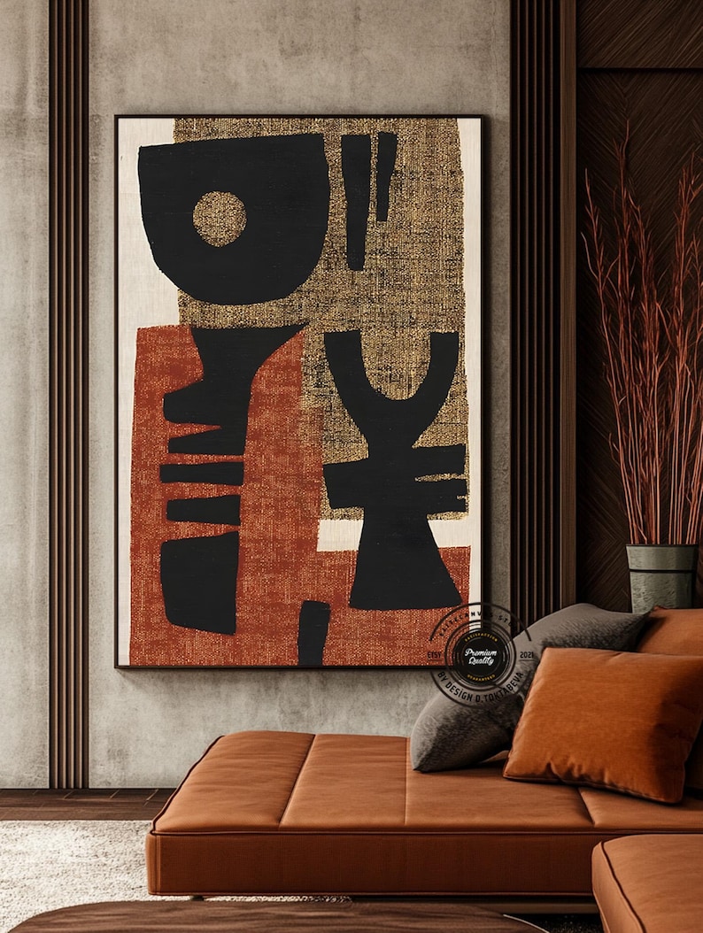 May include: Abstract art print featuring bold black shapes on a textured gold and rust-colored background. The artwork is framed in a black border and hangs above a brown leather sofa with matching throw pillows. The overall aesthetic is modern and minimalist.