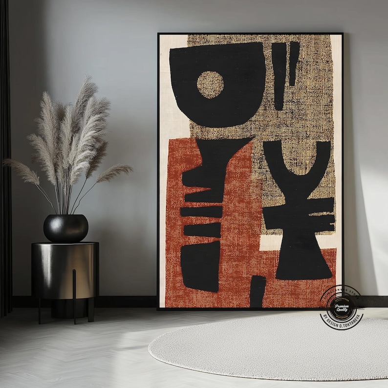 May include: Abstract art print featuring bold black shapes on a textured background of rust, beige, and gold. The artwork is framed in black and displayed in a modern interior setting. The print has a minimalist design.
