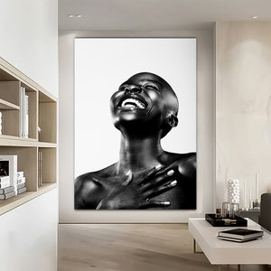 Op de afbeelding: Zwart-wit portret van een persoon met een geschoren hoofd die lacht met het hoofd naar achteren gekanteld. De persoon draagt geen kleding en heeft de handen op de borst gevouwen.