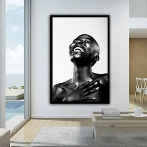 Op de afbeelding: Zwart-wit portret van een persoon met een geschoren hoofd die lacht met het hoofd naar achteren gekanteld. De persoon draagt een simpel zwart shirt en heeft de handen gevouwen over de borst.