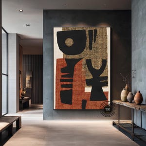 May include: Large abstract canvas art with black, rust, and beige shapes. The artwork features bold geometric forms and textures, creating a modern and minimalist aesthetic. The piece is framed and displayed in a contemporary interior setting.