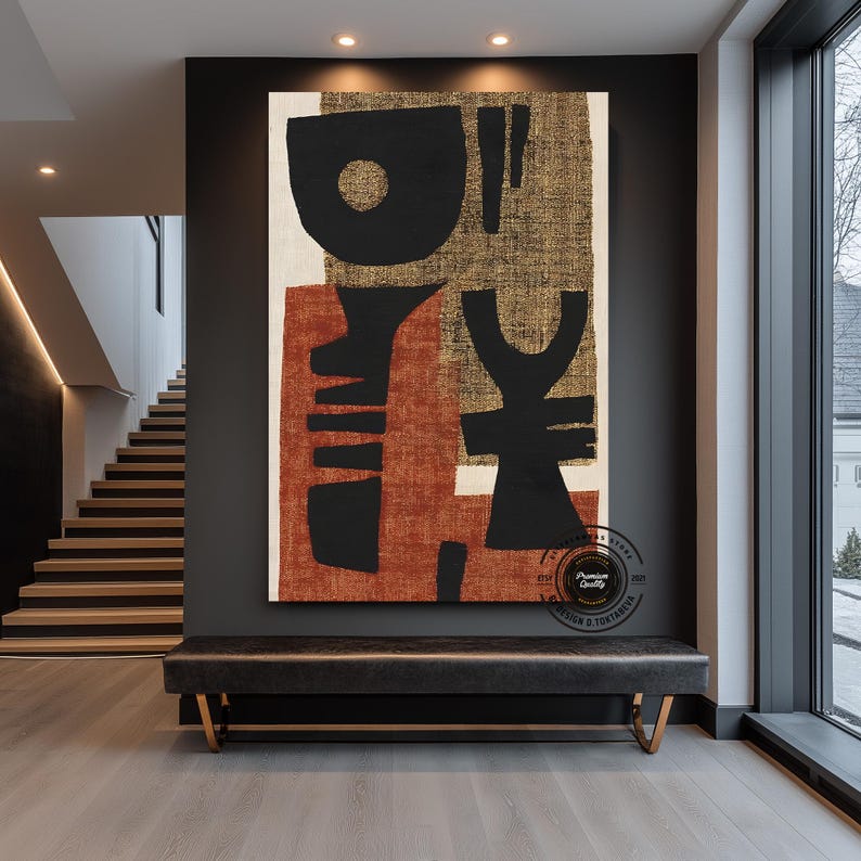 May include: Large abstract canvas art with black, rust, and gold shapes. The artwork hangs above a black leather bench with gold legs in a modern entryway. The art features a mix of geometric and organic forms.