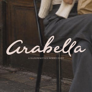 Puede incluir: El texto Arabella se muestra en una fuente de escritura a mano grande y de color rosa claro. Debajo, el texto A HANDWRITTEN SCRIPT FONT está escrito en una fuente sans-serif blanca más pequeña. El fondo muestra a una persona con pantalones oscuros.