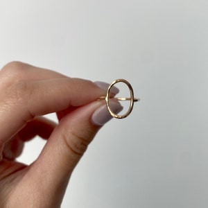 May include: A gold oval ring with a hammered texture. The ring is open and has a simple design.