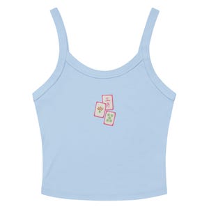 Könnte beinhalten: Hellblaues Tanktop mit dünnen Trägern. Es hat eine kleine Grafik von drei Mahjong-Steinen mit rosa Umrissen und japanischen Schriftzeichen. Die Steine haben Blumen- und Punktmuster. Ein lässiges Oberteil.