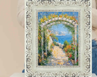 Può includere: Dipinto incorniciato raffigurante una scena costiera con un arco bianco ornato di fiori. L'opera presenta un sentiero che conduce al mare, con colori vivaci di blu, giallo e verde. La cornice è bianca con dettagli ornati.
