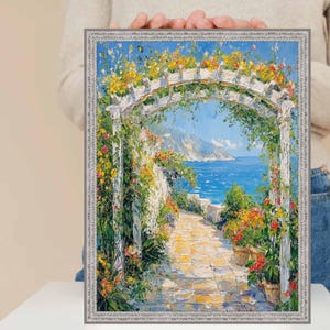 Può includere: Un dipinto a olio incorniciato raffigura una scena costiera con un pergolato bianco adornato da fiori colorati. Un sentiero di pietra conduce al mare sotto un cielo azzurro. Il dipinto è tenuto da una persona.