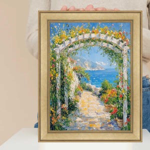 May include: A framed painting of a white archway covered in colorful flowers leading to a path that ends at a blue ocean. The path is made of stone and the ocean is in the background.