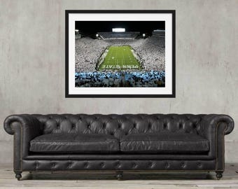 Può includere: Una fotografia incorniciata di uno stadio di calcio pieno di spettatori. Il campo è verde con linee bianche e le parole "PENN STATE" sono visibili. La fotografia è esposta sopra un divano Chesterfield in pelle nera.
